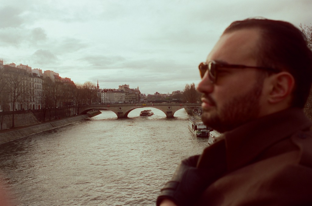 Blurred silhouette of Gabriel walking on a Paris bridge, motion effect.