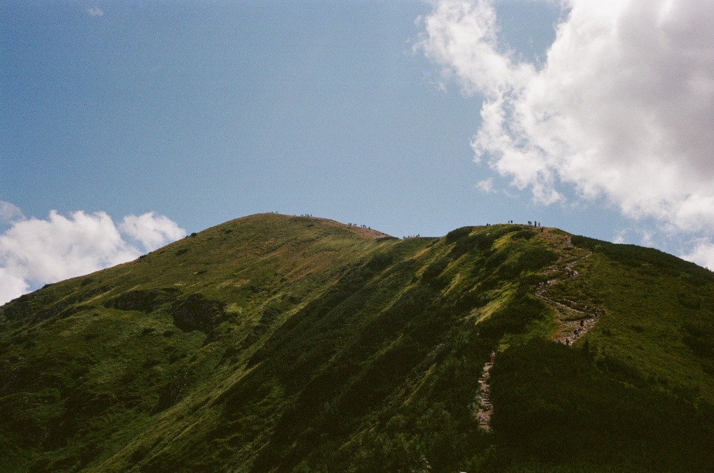 Green mountain landscape with winding path and heavy sky.