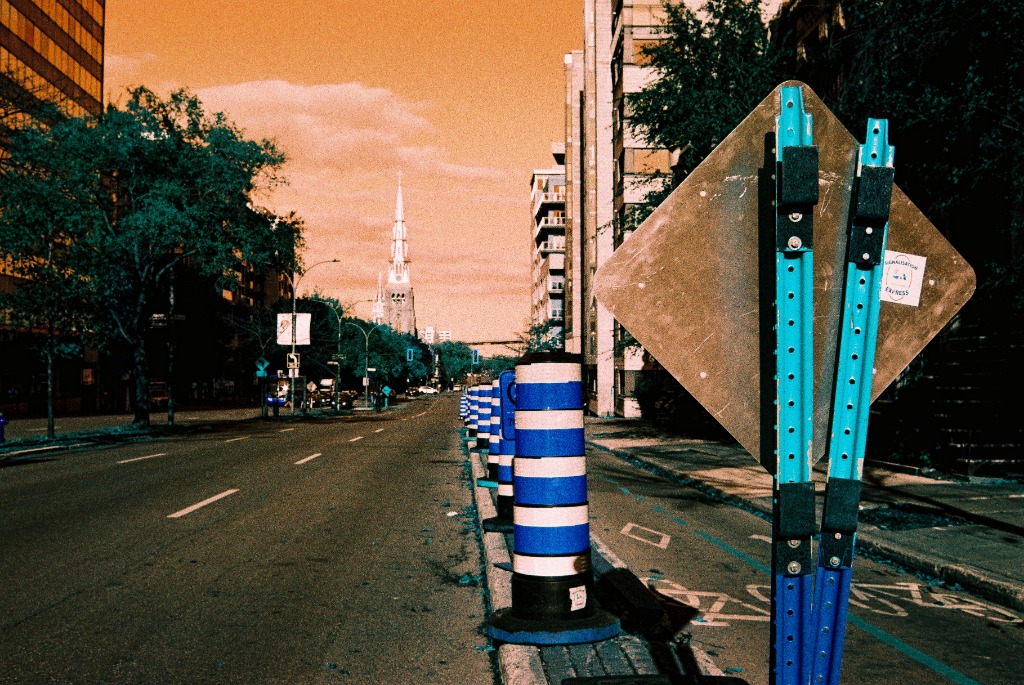 Blue and white construction cones aligned under a sky inverted by LomoChrome Turquoise.