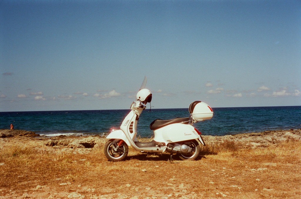 White Vespa parked facing the Adriatic Sea, intense blue sky and ochre earth.