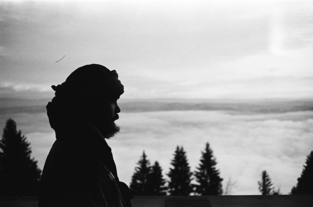 Dark profile silhouette with turban on a balcony overlooking a misty landscape.