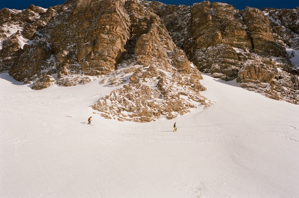 Massive rocky bar towering over two tiny skiers.