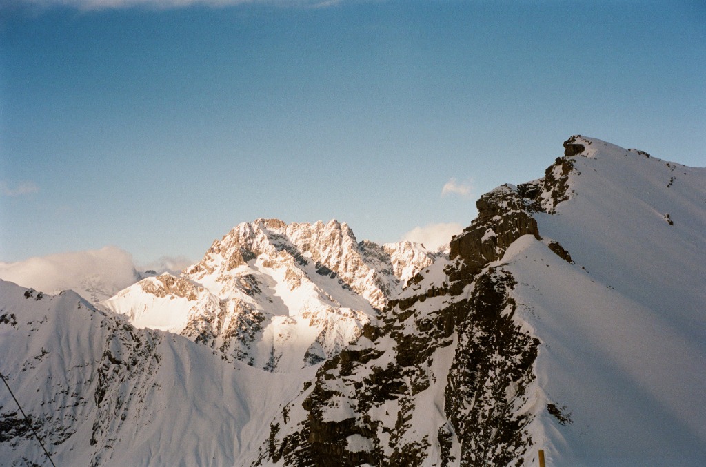 Mountain peak with caramel-colored rocks and white snow under a blue sky.